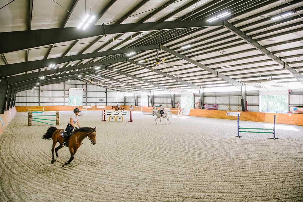 The 100' x 200' Indoor Riding Arena contains dust-free footing and is filled with natural light from large garage doors. The arena also has large fans and no-shadow lighting. 
